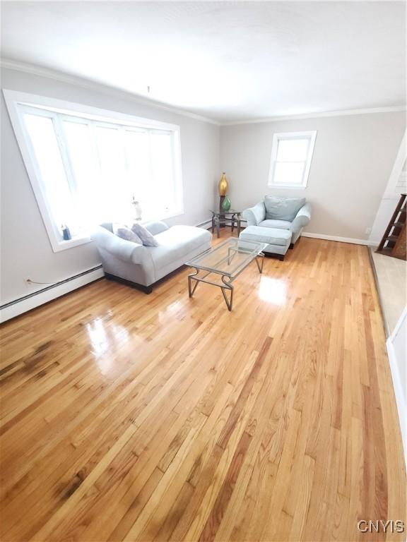 unfurnished living room featuring a baseboard heating unit, crown molding, and wood finished floors