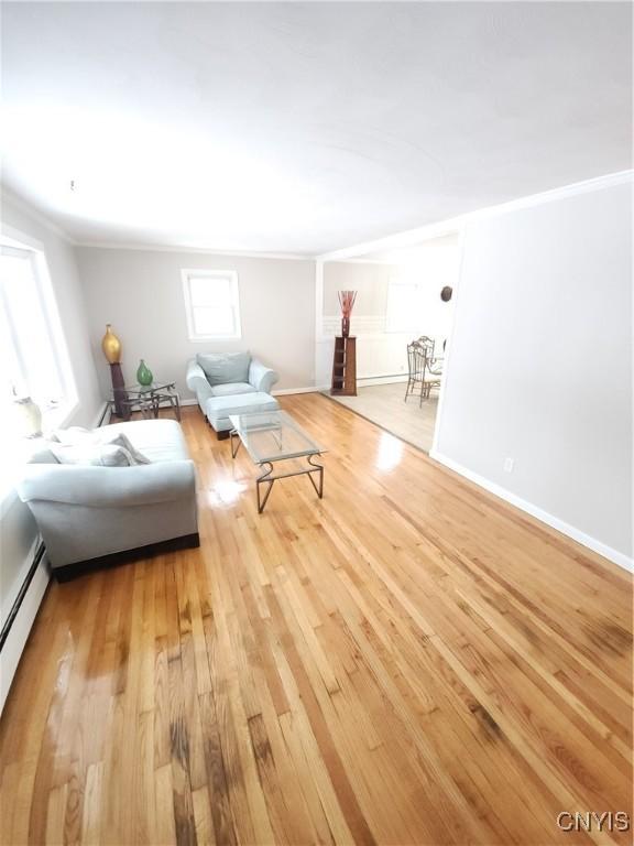 unfurnished living room featuring crown molding, a baseboard radiator, wood finished floors, and baseboards