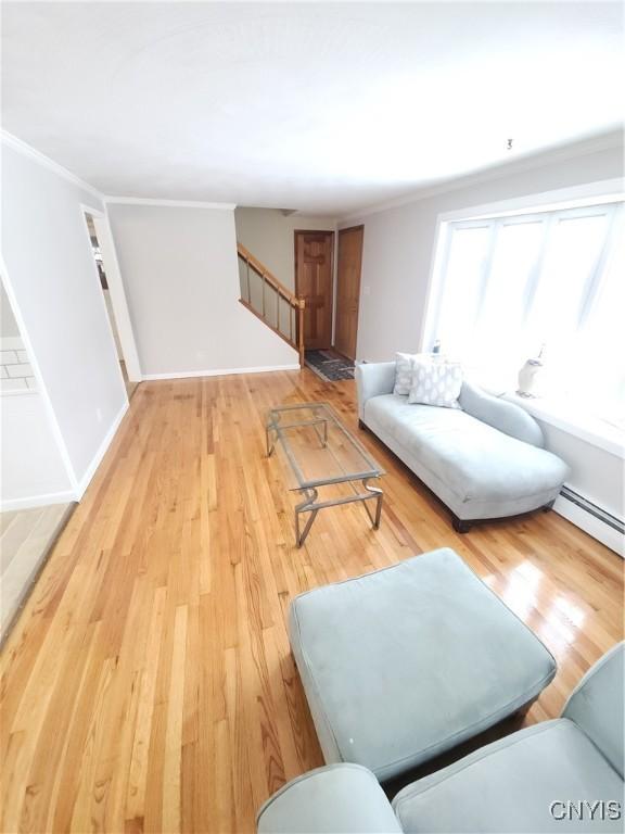 living area with ornamental molding, light wood-type flooring, stairway, and a baseboard radiator