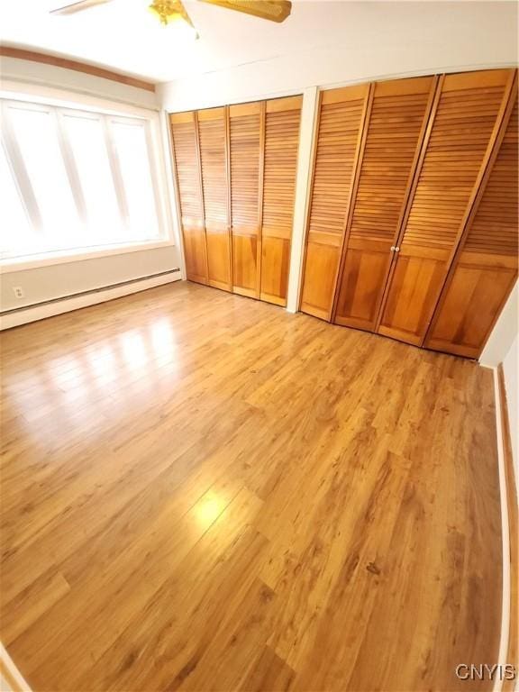 unfurnished bedroom featuring ceiling fan, baseboard heating, multiple closets, and light wood-style floors