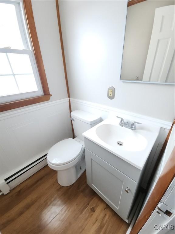 half bath featuring toilet, a baseboard radiator, wood finished floors, and vanity