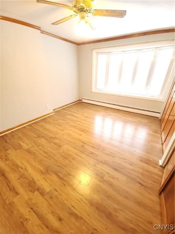 empty room with light wood finished floors, baseboard heating, ornamental molding, ceiling fan, and baseboards