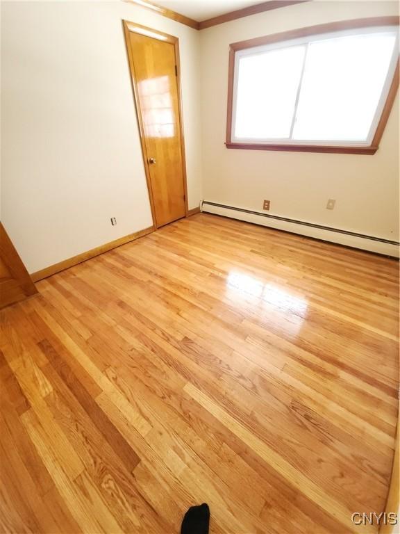 spare room featuring a baseboard radiator, baseboards, light wood-style flooring, and crown molding