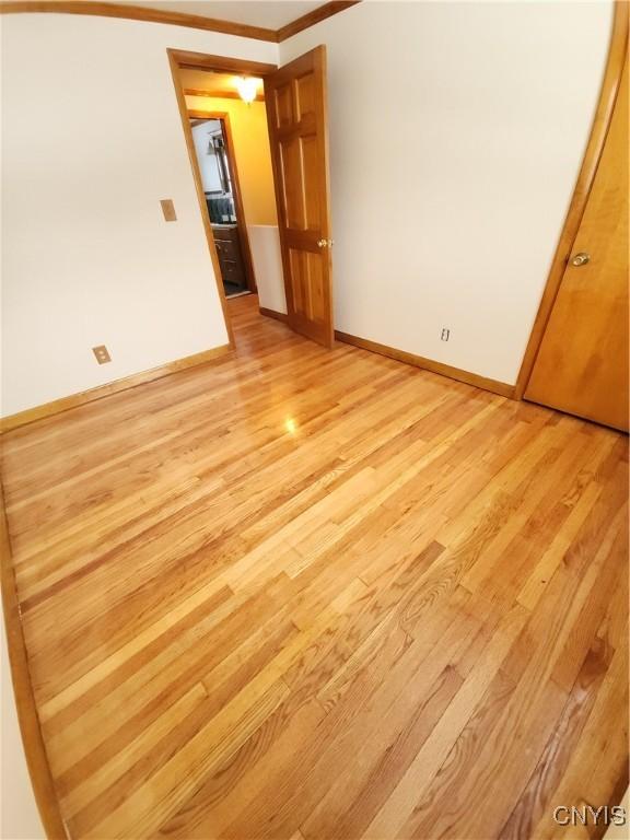 spare room with light wood-style floors, baseboards, and crown molding