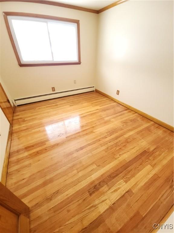 unfurnished room featuring light wood-style flooring, ornamental molding, baseboard heating, and baseboards