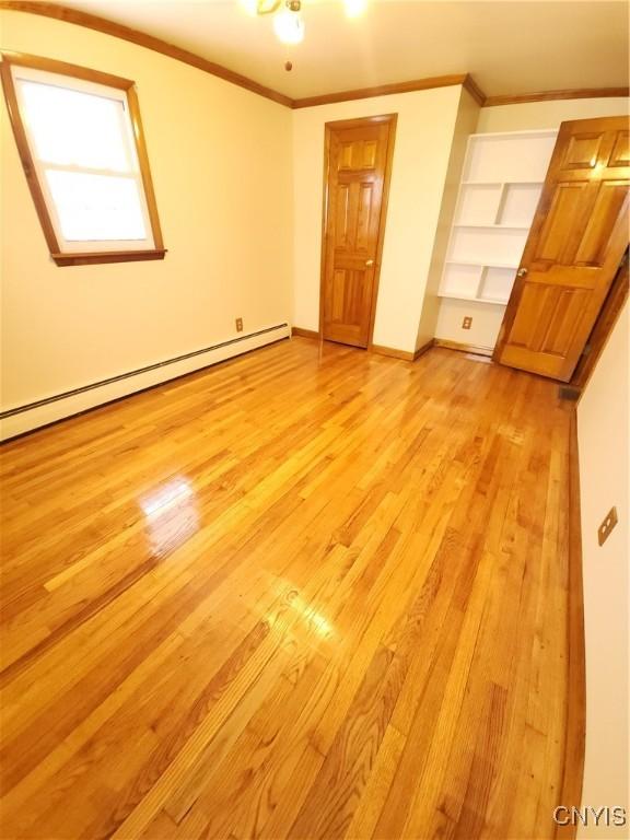 unfurnished bedroom featuring a baseboard heating unit, ornamental molding, light wood-style flooring, and baseboards