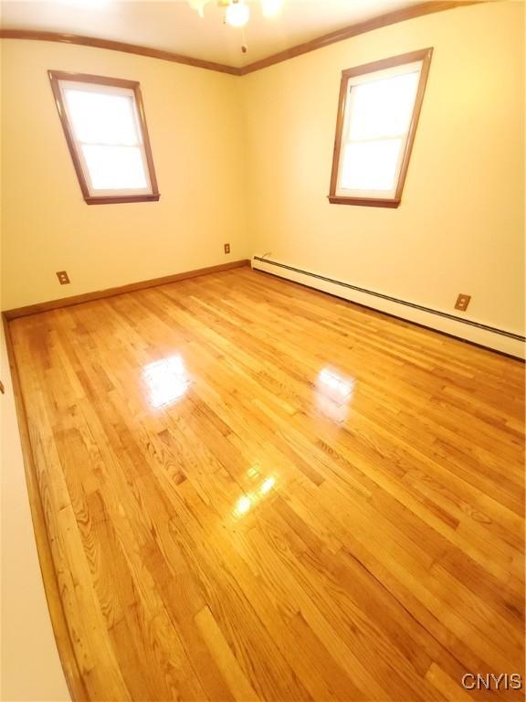 spare room with a baseboard heating unit, light wood-type flooring, crown molding, and baseboards