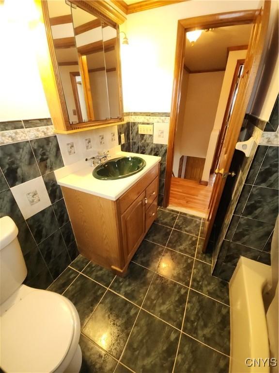 bathroom with toilet, a wainscoted wall, vanity, tile walls, and tile patterned floors