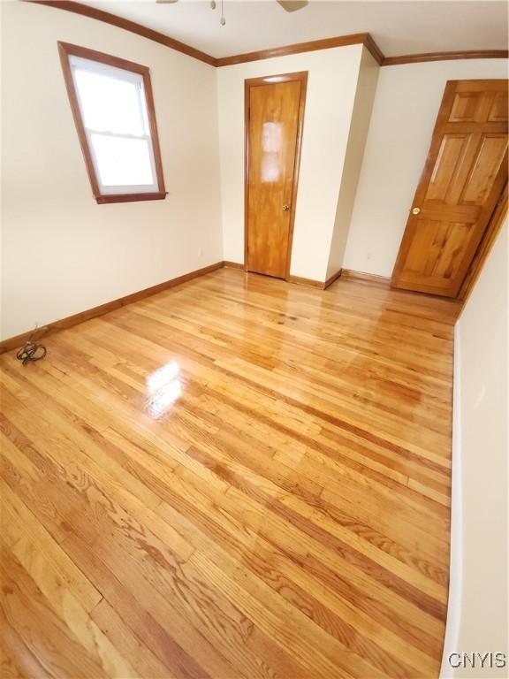 unfurnished room with light wood finished floors, baseboards, and crown molding