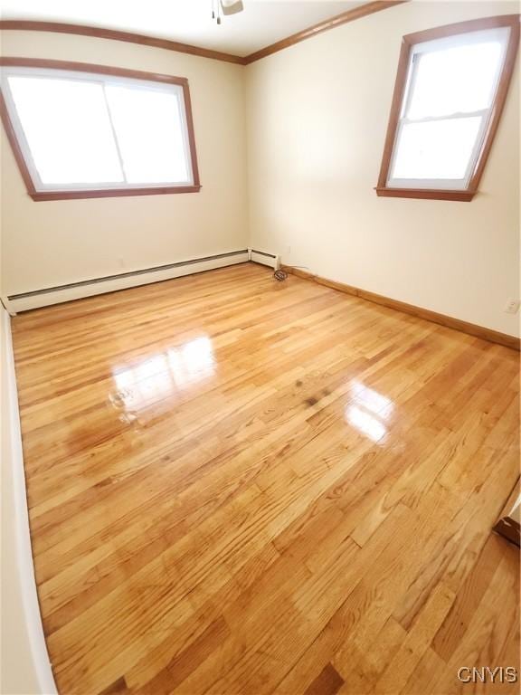 empty room featuring baseboards, a ceiling fan, crown molding, light wood-type flooring, and a baseboard heating unit