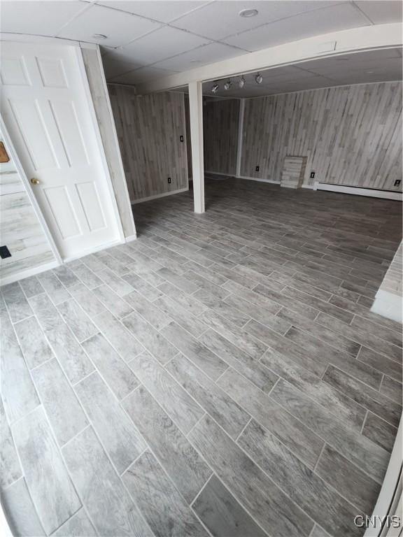 finished basement featuring a baseboard heating unit, wood finish floors, a drop ceiling, and wooden walls