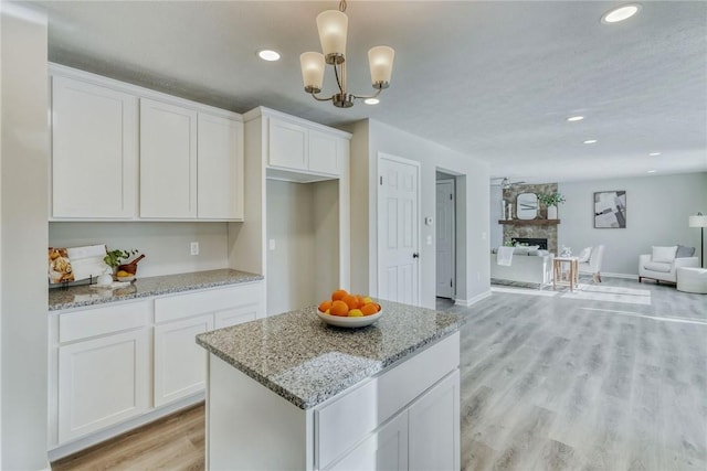 kitchen with open floor plan, a stone fireplace, light wood-type flooring, white cabinetry, and recessed lighting