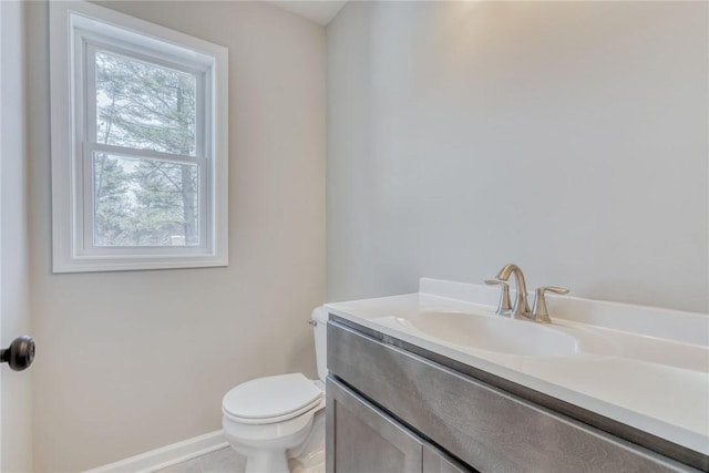 half bath with baseboards, vanity, and toilet