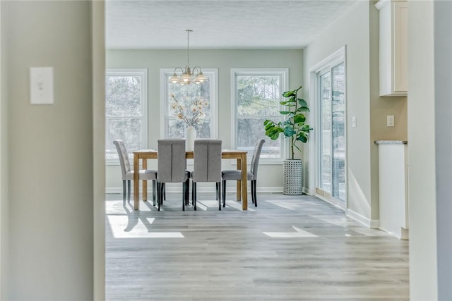 dining space featuring baseboards, a notable chandelier, light wood-style flooring, and a textured ceiling