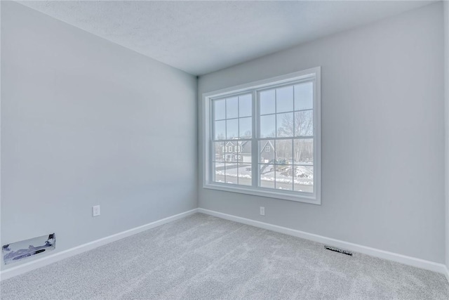 empty room with carpet floors, visible vents, a textured ceiling, and baseboards