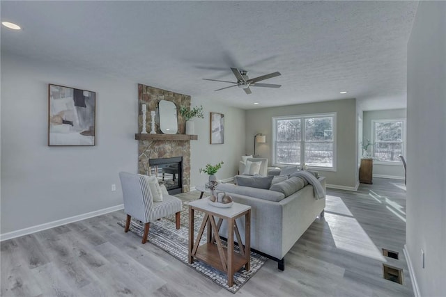 living room featuring baseboards, a stone fireplace, a textured ceiling, and wood finished floors