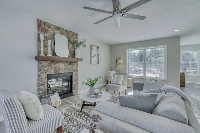 living room with a textured ceiling, a stone fireplace, wood finished floors, and baseboards