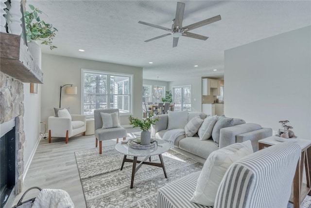 living room featuring a ceiling fan, a premium fireplace, a textured ceiling, light wood-type flooring, and recessed lighting