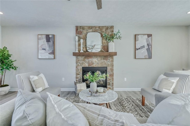 living area featuring a stone fireplace, baseboards, and wood finished floors