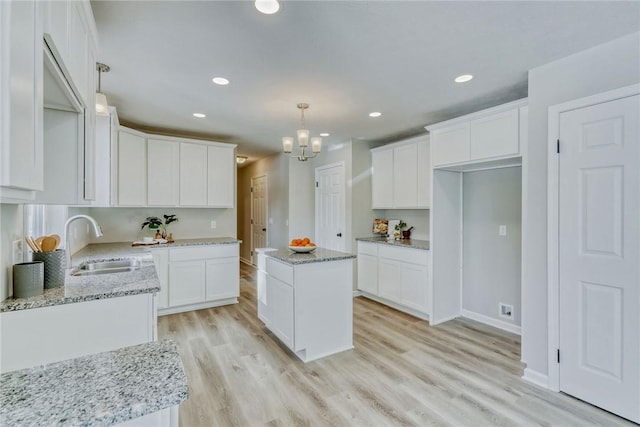 kitchen with light stone countertops, light wood finished floors, a sink, and a center island