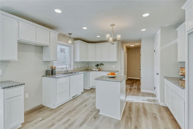 kitchen with light stone counters, light wood-type flooring, a sink, and white cabinets