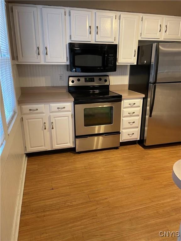 kitchen with stainless steel appliances, light wood-type flooring, white cabinets, and light countertops