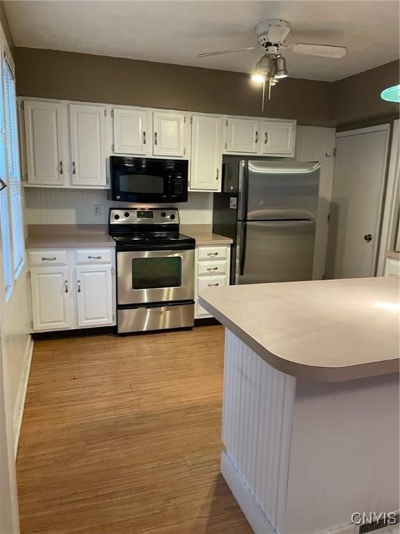 kitchen with electric range, wood finished floors, freestanding refrigerator, light countertops, and black microwave