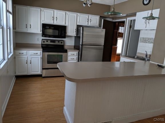 kitchen featuring stainless steel appliances, a peninsula, a sink, white cabinetry, and light countertops