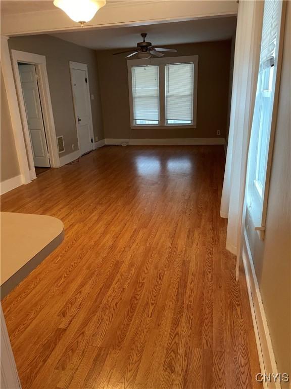 unfurnished living room featuring light wood-type flooring, baseboards, and a ceiling fan