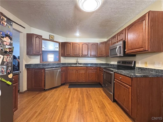 kitchen featuring a textured ceiling, a sink, appliances with stainless steel finishes, light wood-type flooring, and dark countertops