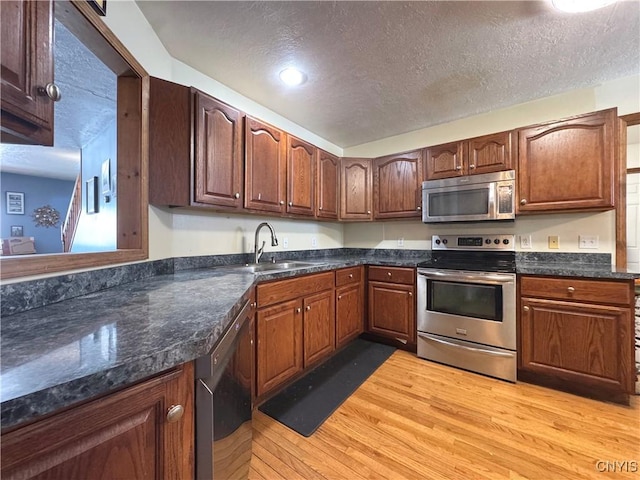 kitchen featuring light wood finished floors, a textured ceiling, appliances with stainless steel finishes, and a sink