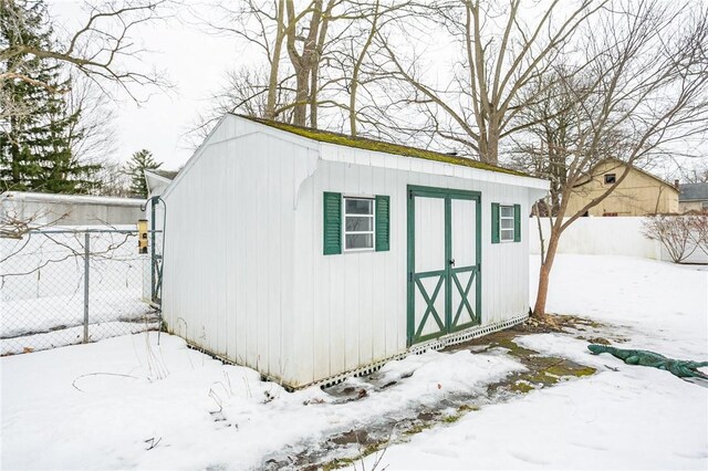 snow covered structure featuring an outdoor structure, a storage shed, and fence