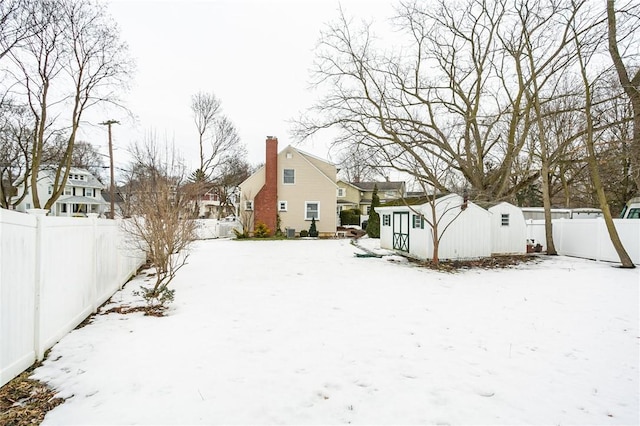 snow covered property with a fenced backyard, a residential view, a chimney, and an outdoor structure