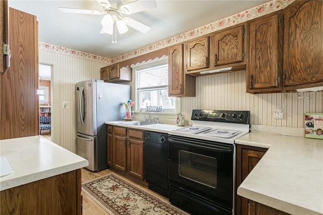 kitchen featuring a sink, a ceiling fan, light countertops, black appliances, and wallpapered walls