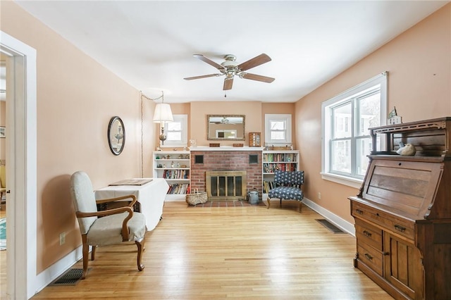 living area featuring ceiling fan, a fireplace, visible vents, baseboards, and light wood-style floors