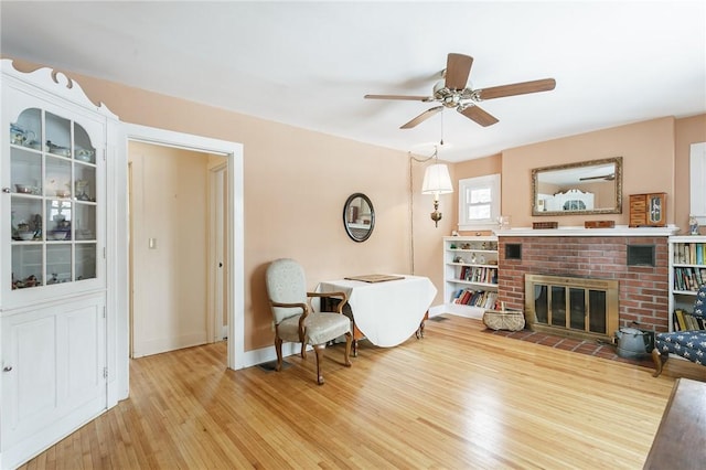 interior space featuring ceiling fan, a fireplace, baseboards, and wood finished floors