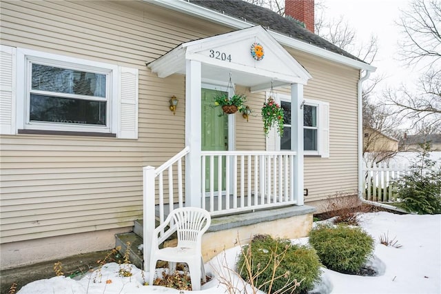 snow covered property entrance featuring a chimney and fence