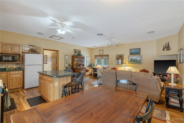 dining space with light wood-style flooring, a ceiling fan, and visible vents