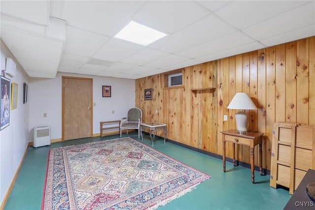 living area with a drop ceiling, wood walls, finished concrete flooring, and baseboards