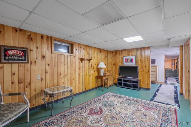 living area featuring concrete flooring, a drop ceiling, baseboards, and wooden walls