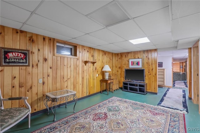 sitting room with a drop ceiling, baseboards, finished concrete floors, and wood walls