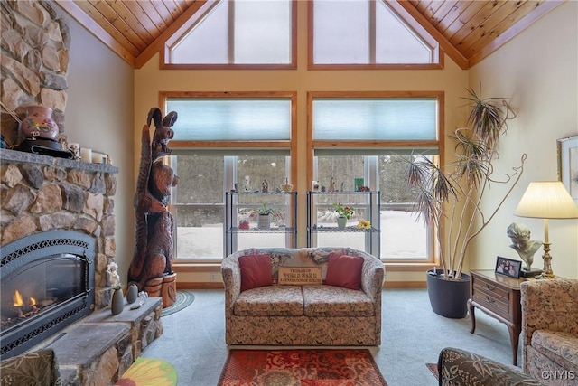 living area with carpet floors, a stone fireplace, baseboards, wood ceiling, and vaulted ceiling