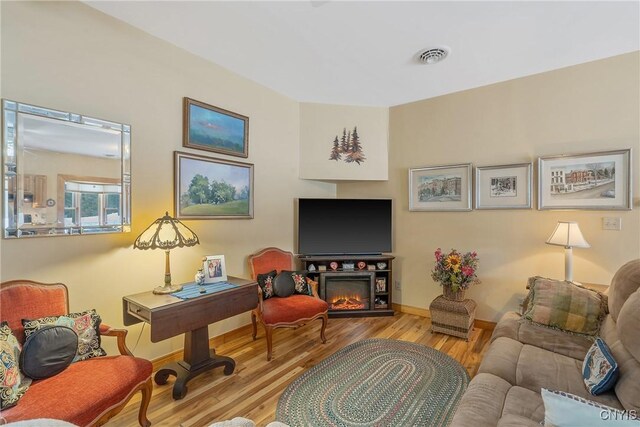 living area featuring a warm lit fireplace, baseboards, visible vents, and wood finished floors