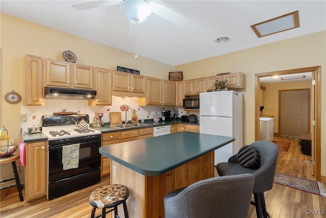 kitchen with dark countertops, a sink, light wood-type flooring, white appliances, and under cabinet range hood