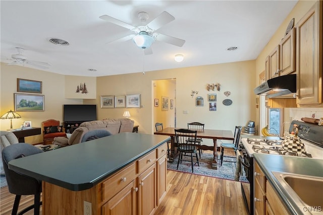 kitchen with range with gas stovetop, dark countertops, a ceiling fan, and under cabinet range hood