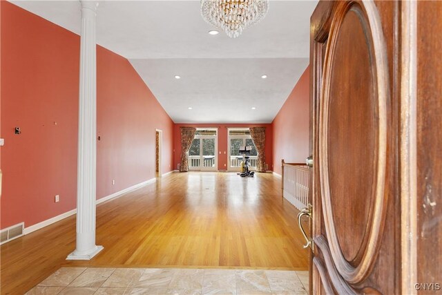 unfurnished living room with light wood finished floors, baseboards, visible vents, lofted ceiling, and ornate columns