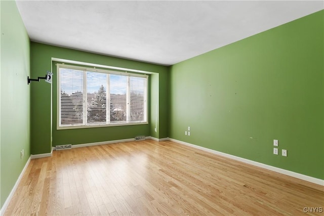 empty room featuring baseboards, visible vents, and wood finished floors