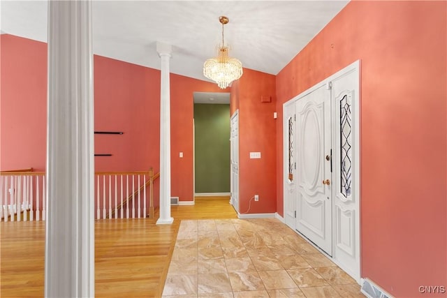 entryway with a notable chandelier, ornate columns, vaulted ceiling, wood finished floors, and baseboards