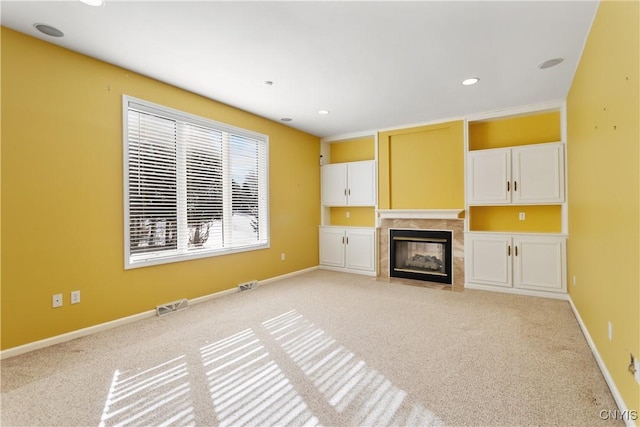 unfurnished living room featuring light colored carpet, visible vents, baseboards, and a premium fireplace