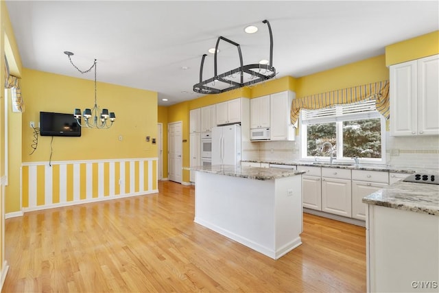 kitchen with white appliances, a kitchen island, white cabinets, and light wood-style floors